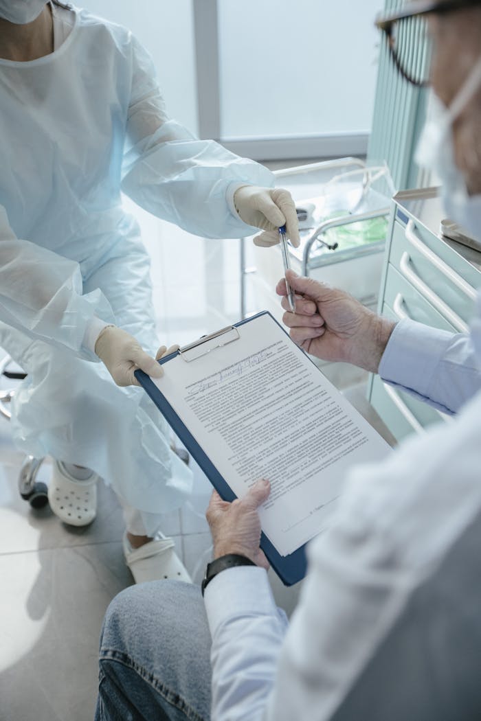 gallery-4 A patient in a medical office receives a document to sign from a healthcare professional for processing.